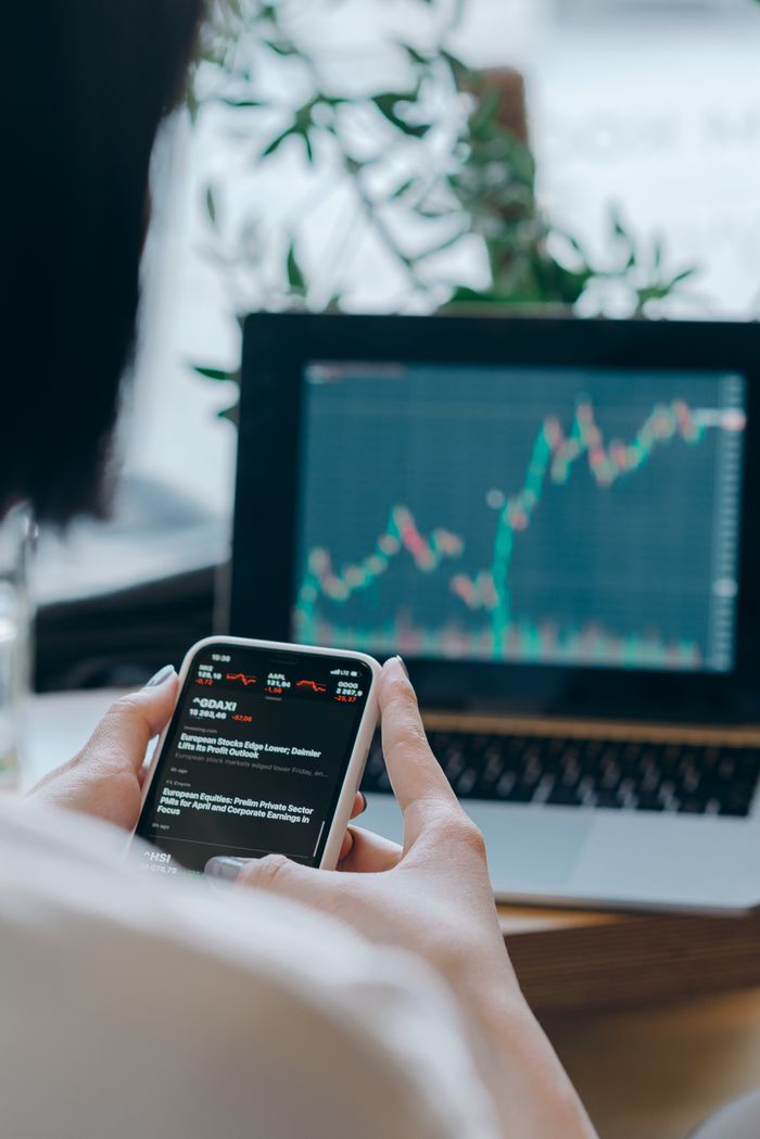 project-01-b Person using smartphone for stock market analysis at home office.