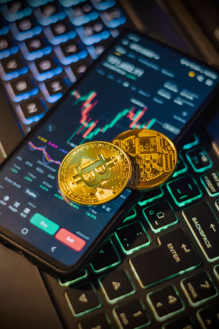 project-03-b Cryptocurrency trading interface on a mobile with Bitcoin coins on a laptop keyboard.